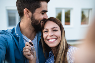 Happy young couple with key standing outside in front of their new home.