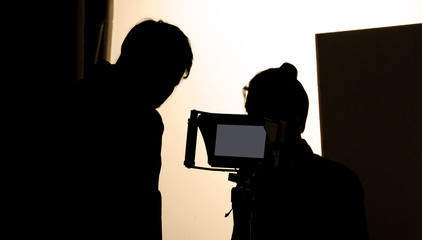 Shooting studio behind the scenes in silhouette images which film crew team working for filming movie or video with professional lighting and equipment such as camera, tripod, soft box, monitor