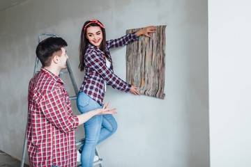 happy couple doing a home makeover and painting walls, the woman is using a paint roller and the man