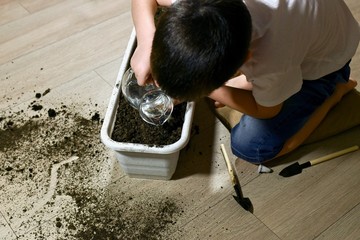 A child pours soil in pots while sitting next to him on his lap.