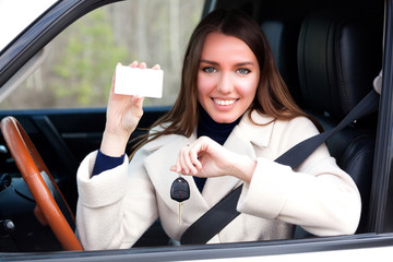 Happy girl in a car showing a key and an empty white card for your text