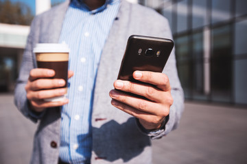 Businessman using phone and holding cup of coffee,close up