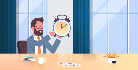 happy businessman holding alarm antique clock business man sitting workplace desk deadline time management concept modern office interior male cartoon character portrait flat