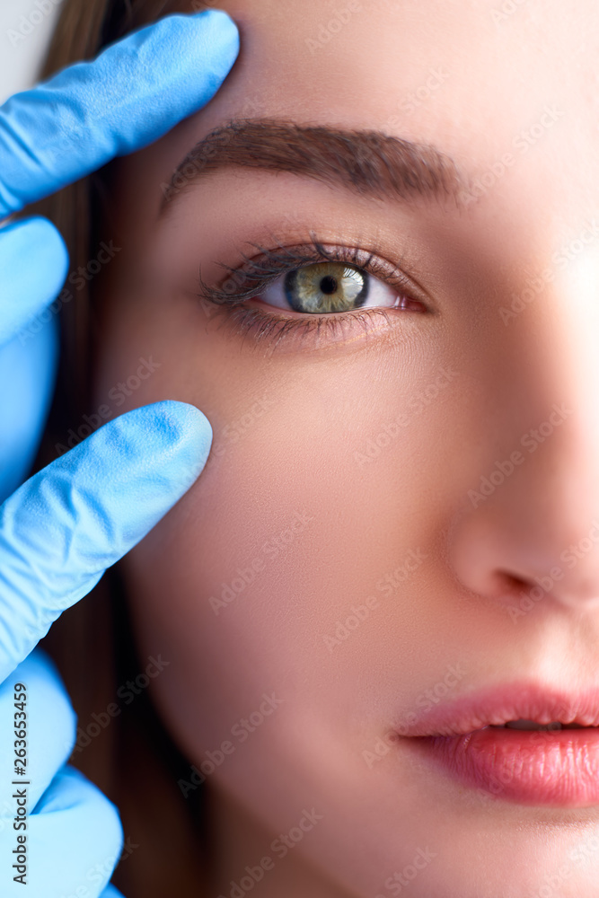 Upper eyelid reduction, double eye lid removal plastic surgery concept. Beautician doctor hands in gloves touching female face skin. Ophthalmologist or oculist checks healthy vision in green eyesight. - obrazy, fototapety, plakaty 