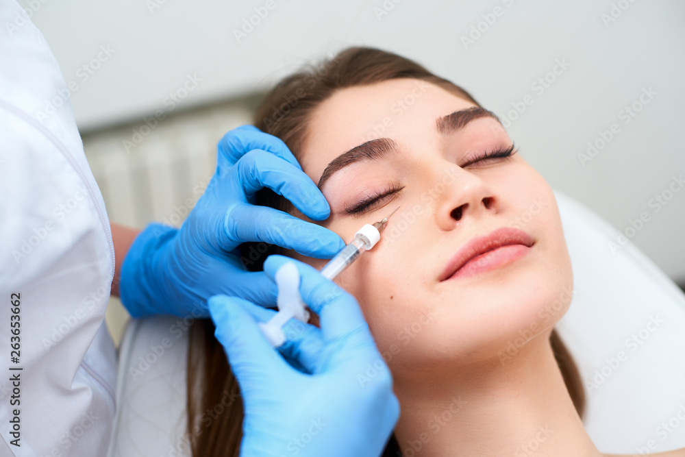 Doctor in medical gloves with syringe injects botulinum under eyes for rejuvenating wrinkle treatment. Filler injection for eye wrinkles smoothing. Plastic aesthetic facial surgery in beauty clinic