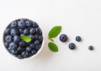 Wall Mural - Fresh raw organic blueberries with leaf in white china bowl on white background. Top view. Space for text