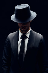 Wall Mural - Handsome confident man in black suit and hat on dark background