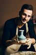 © GVS - Smiling handsome man showing handmade ceramic pot at pottery workshop