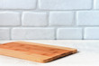 Background kitchen with cutting board on white wooden table and against the background a brick wall.
