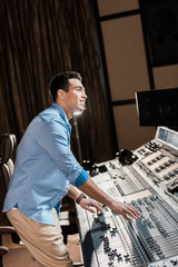 Canvas Print - smiling mixed race musician working at mixing console in recording studio