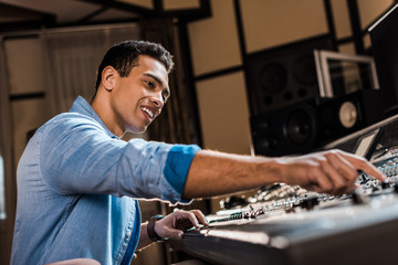 Canvas Print - selective focus of smiling mixed race sound producer working at mixing console in recording studio