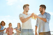 © Friends Stock - Cheers to us! Two smiling young men clinking glasses with beer and looking at each other while standing on the roof with friends.
