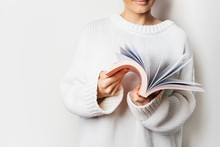 Close View Of Woman In White Woolen Sweater Holding An Open Book With Pink Cover In Hands. Mock Up Of Reading Book Concept Background.