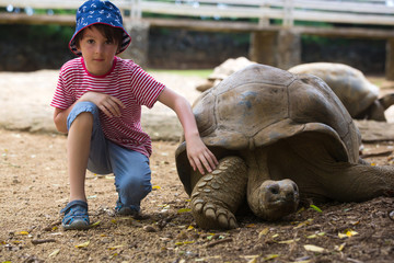 Happy family, children and parents, feeding giant tortoises in a exotic park on Mauritius island