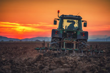 Beautiful Sunset, Farmer In Tractor Preparing Land With Seedbed Cultivator