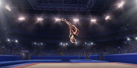 Wall Mural - Female athlete doing a complicated exciting jump trick in a professional gym. Girl perform stunt in bright sports clothes