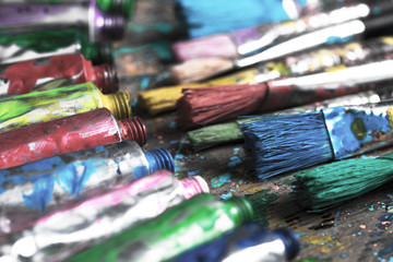 Stained paintbrushes and acrylic pain tubes on artist table. Artistic background