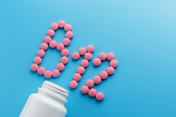 Pink pills in the shape of the letter B12 on a blue background, spilled out of a white can.