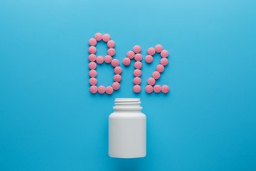 Pink pills in the shape of the letter B12 on a blue background, spilled out of a white can.