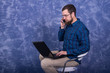 © mihakonceptcorn - Cheerful young man working on laptop seated on a chair isolated over white background. Creative freelancer guy working from home at his notebook computer, full body length portrait.