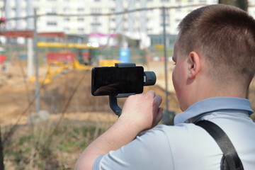 Wall Mural - A young man videotaping on a smartphone. Uses gimbal to get smooth footage. Closely watching the movie shooting.