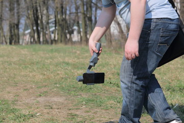 Wall Mural - A young man videotaping on a smartphone. Uses gimbal to get smooth shots. Keeps record low on the ground.