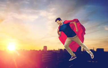 Wall Mural - super power and people concept - happy young man in red superhero cape flying in air over sunset in city background