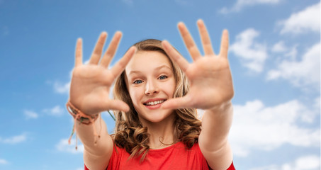 Poster - people concept - smiling teenage girl with long hair in red t-shirt giving high five over blue sky and clouds background