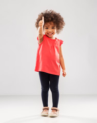 Wall Mural - childhood, gesture and people concept - happy little african american girl showing thumbs up over grey background