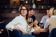 Portrait of gorgeous brunette looking away and holding glass with red wine while sitting at restaurat. In background friends eating diner.