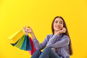 Sticker - Happy young woman with shopping bags on color background