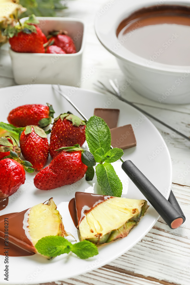 Plate with fresh pineapple, strawberry and melted chocolate on white table
