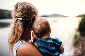 a rear view of mother with a toddler daughter outdoors by the river in summer.