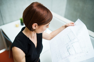 Wall Mural - Young businesswoman or architect with blueprints standing in office.