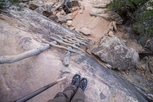 Looking Down An Old Wooden Ladder Leaning Against A Rocky Cliff, First Person Perspective Photo.