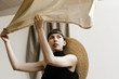© Nicole Mason/Stocksy - fashion model wearing large hat in studio holding sheer gold fabric