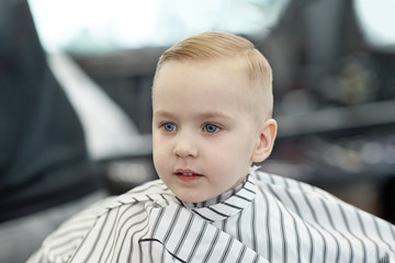 cute blond smiling baby boy with blue eyes in a barber shop after haircut by hairdresser. children f