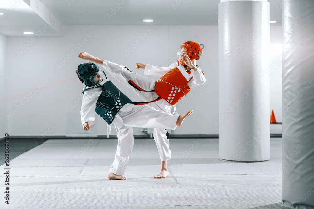 Foto Sporty Caucasian boys having taekwondo training in white gym and kicking each other