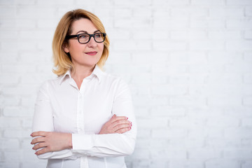 Wall Mural - mature business woman in eyeglasses posing over white brick wall with copy space