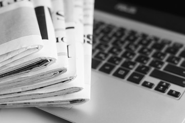 Newspapers and laptop. Pile of daily papers with news on the computer. Pages with headlines, articles folded and stacked on keypad of electronic device. Modern gadget and old journals, focus on paper