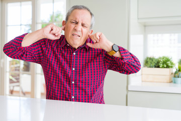 Wall Mural - Handsome senior man at home covering ears with fingers with annoyed expression for the noise of loud music. Deaf concept.