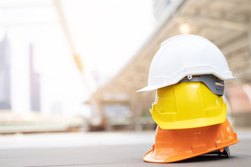 orange yellow and white hard safety wear helmet hat in the project at construction site building on concrete floor on city with sunlight. helmet for workman as engineer or worker. concept safety first