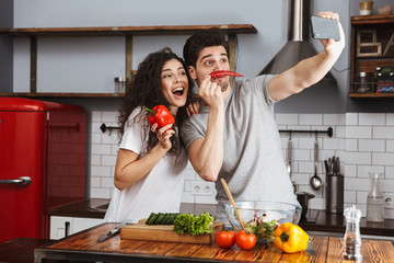 Sticker - Picture of caucasian couple taking selfie photo while cooking salat with vegetables together in modern kitchen at home