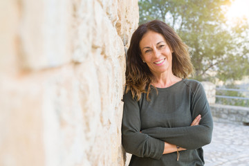 Poster - Beautiful middle age woman smiling cheerful leaning on a brick wall at the city street on a sunny day