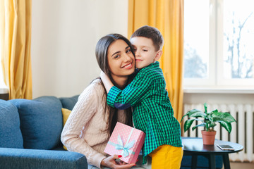 Happy mother hugging her adorable little son and holding gift box. Mothers Day