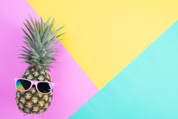 Beach accessories pineapple with pink sunglasses on pink, green and yellow background for summer holiday and vacation concept.