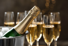 Bottle Of Champagne In Bucket With Ice And Glasses On Blurred Background, Closeup. Space For Text