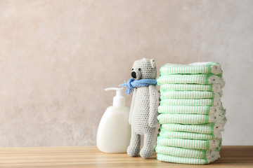 Wall Mural - stack of diapers, toy bear and cream on table against color background, space for text. baby accesso