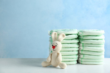 Wall Mural - stacks of diapers and toy bunny on table against color background, space for text. baby accessories