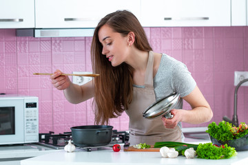 Wall Mural - Cooking woman tasting dish in kitchen at home. Cooking preparation for family for dinner. Clean healthy food and proper nutrition.